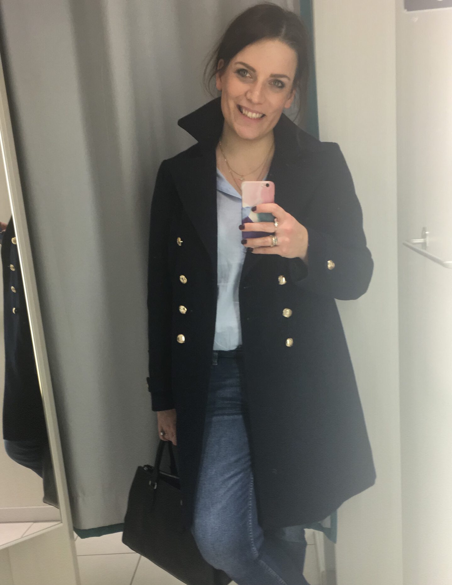 Junge Frau im blauen Mantel macht ein Selfie in der Umkleidekabine.